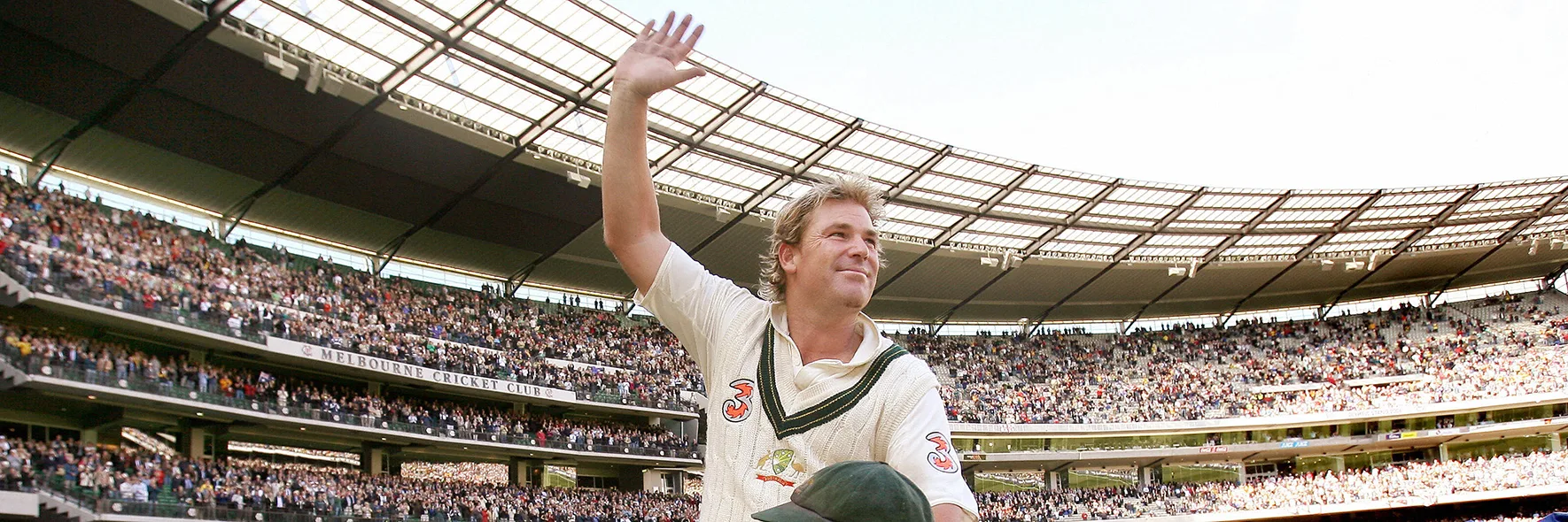 Cricketer Shane Warne waving to huge MCG crowd as he's carried by teammates.