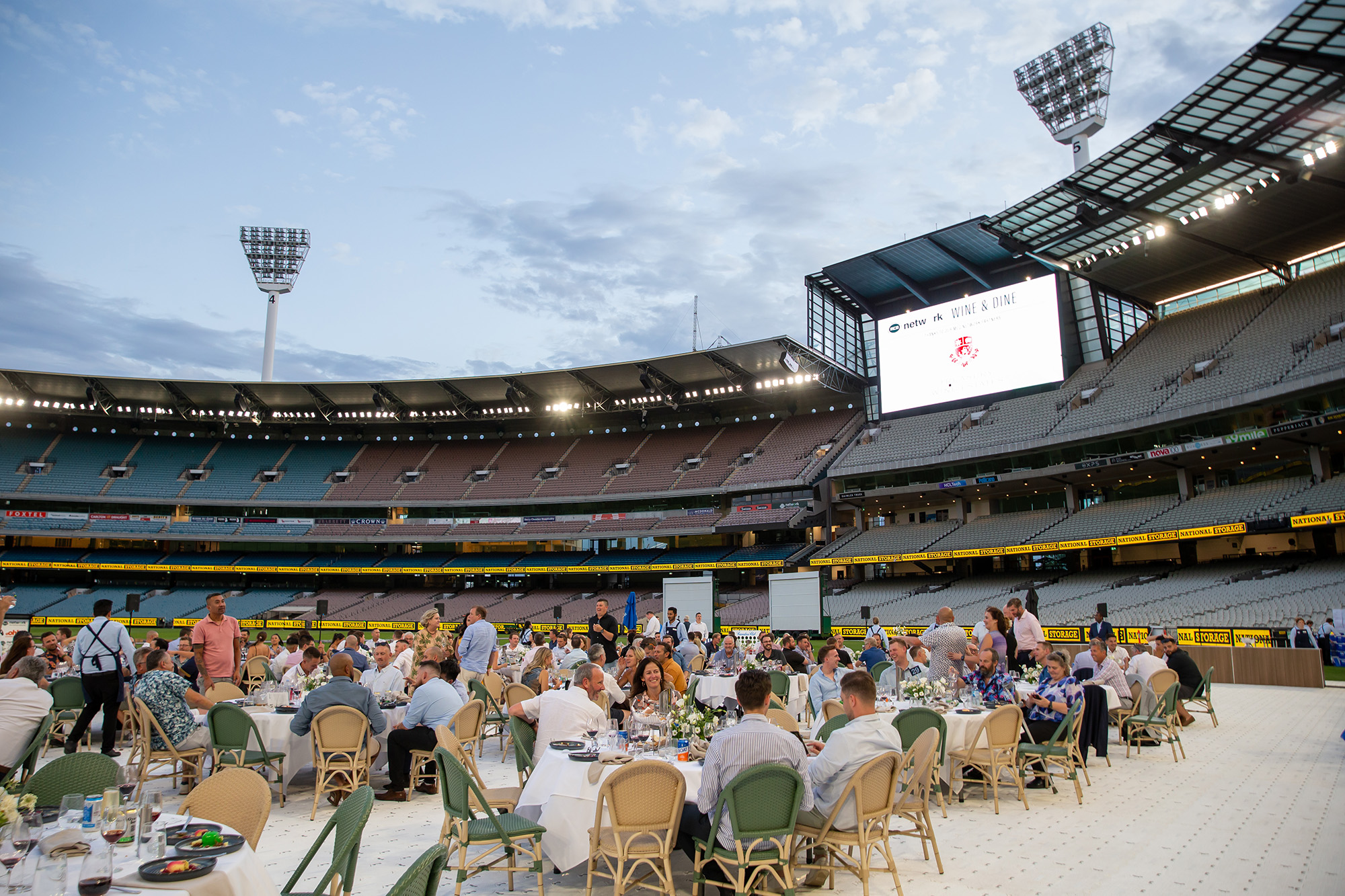 People dining on the MCG with the stands and light towers in the background