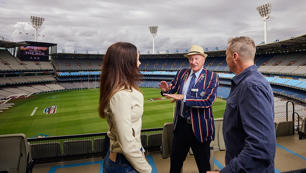 Tour guide speaks with two visitors overlooking MCG arena