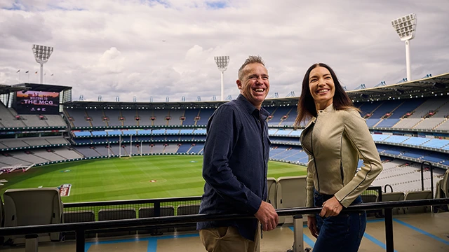 Two visitors smile from an upper-level seating area overlooking the MCG arena