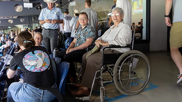 A busy stadium with a person using a wheelchair in a dedicated space. They smile next to a companion.