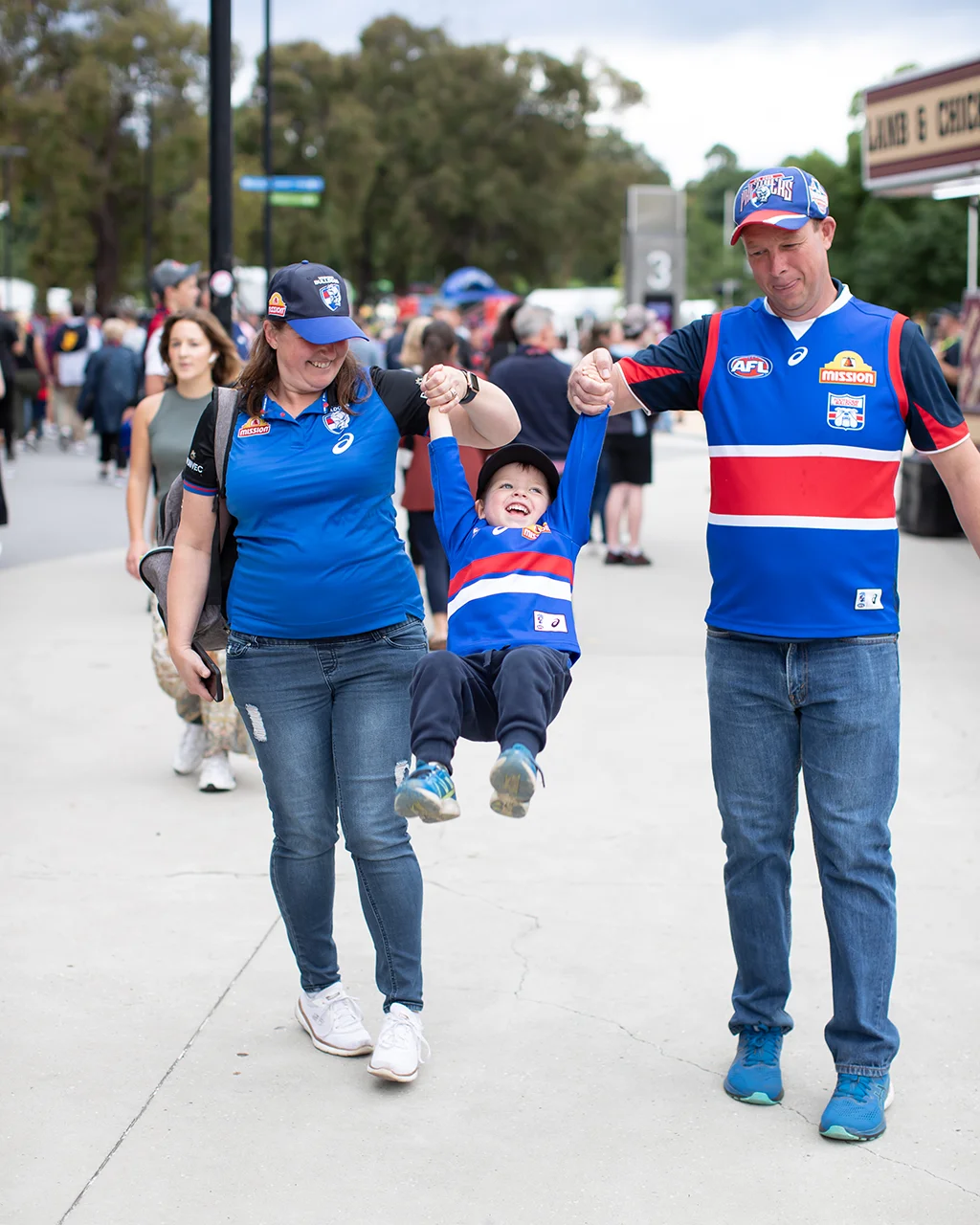 Adults and a young child in AFL merch play together on a busy concourse.