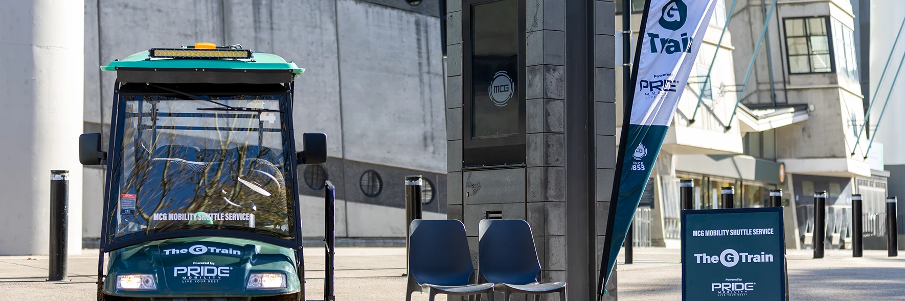 A buggy outside a stadium. It's parked next to chairs and a sign for the G Train, MCG Mobility Shuttle Service
