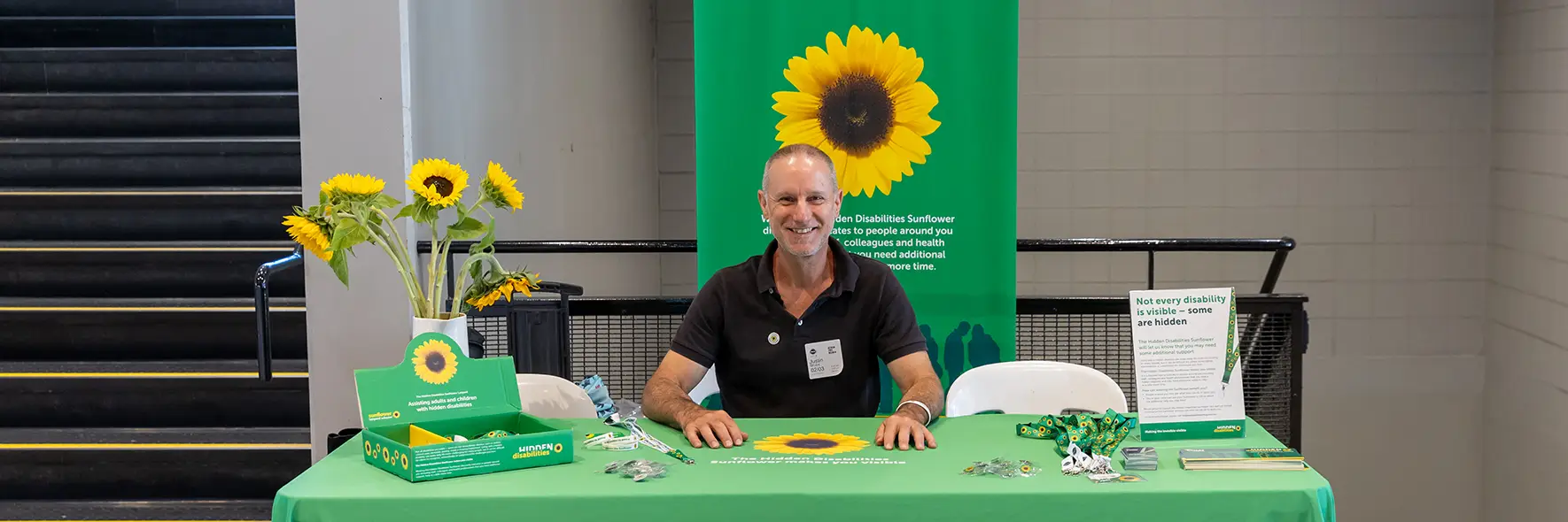 Staff member at a table display about the Hidden Disabilities Sunflower
