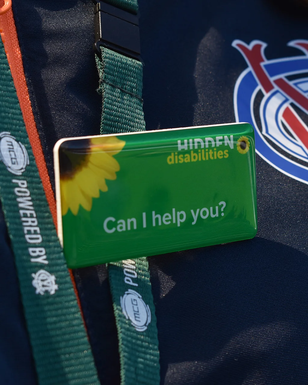 MCG staff member wears a Hidden Disabilities badge that reads 'Can I help you?'