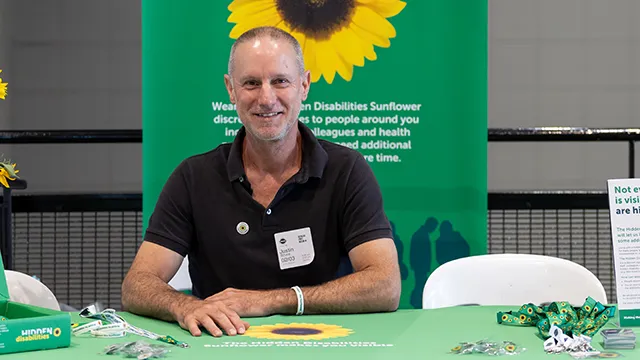 Staff member at a table display about the Hidden Disabilities Sunflower