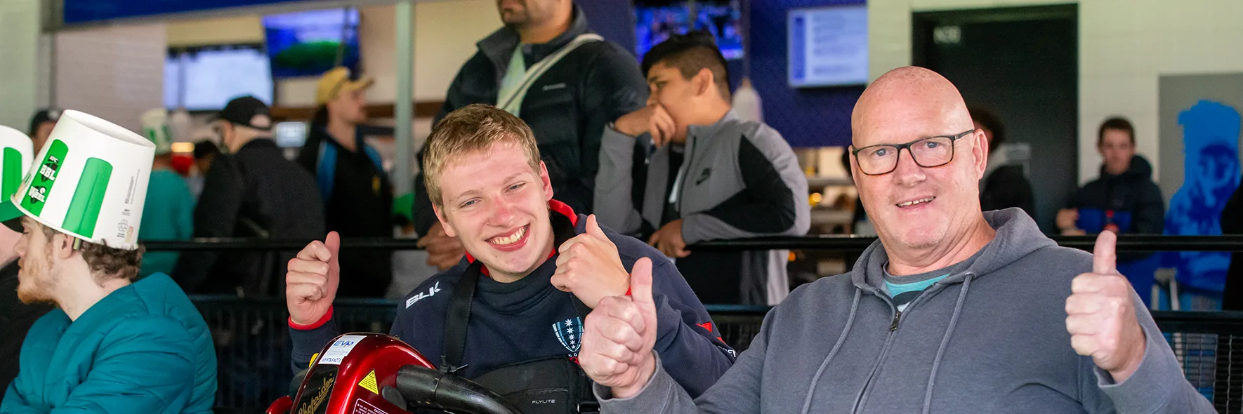 nside a stadium seating bowl with two patrons, one using a mobility scooter. Both people are smiling with thumbs up.