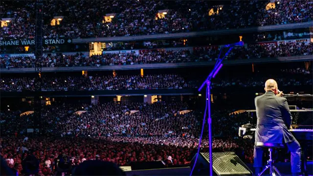 Musician under a bright light performs to a large crowd