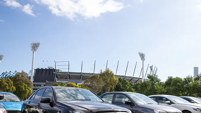 Row of cars in parkland in front of the MCG