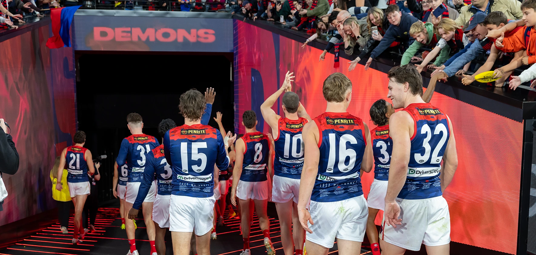 Melbourne FC players walking off the MCG through the players' tunnel, high-fiving fans