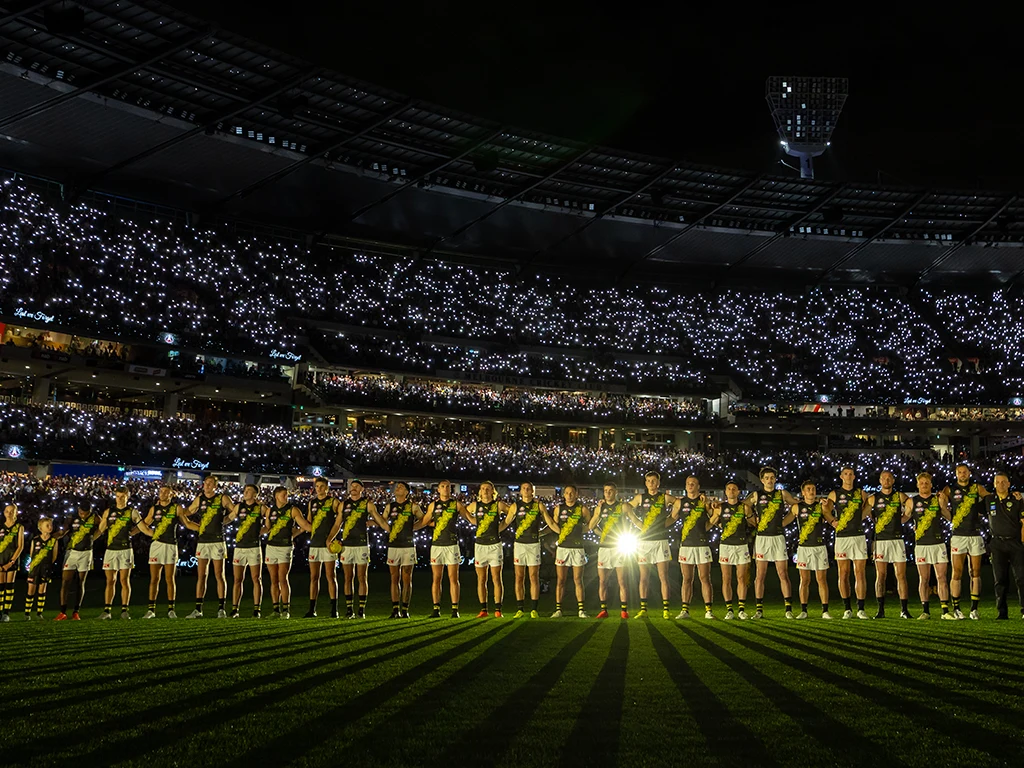Richmond players during ANZAC Day Eve pre-match ceremony with MCG in darkness